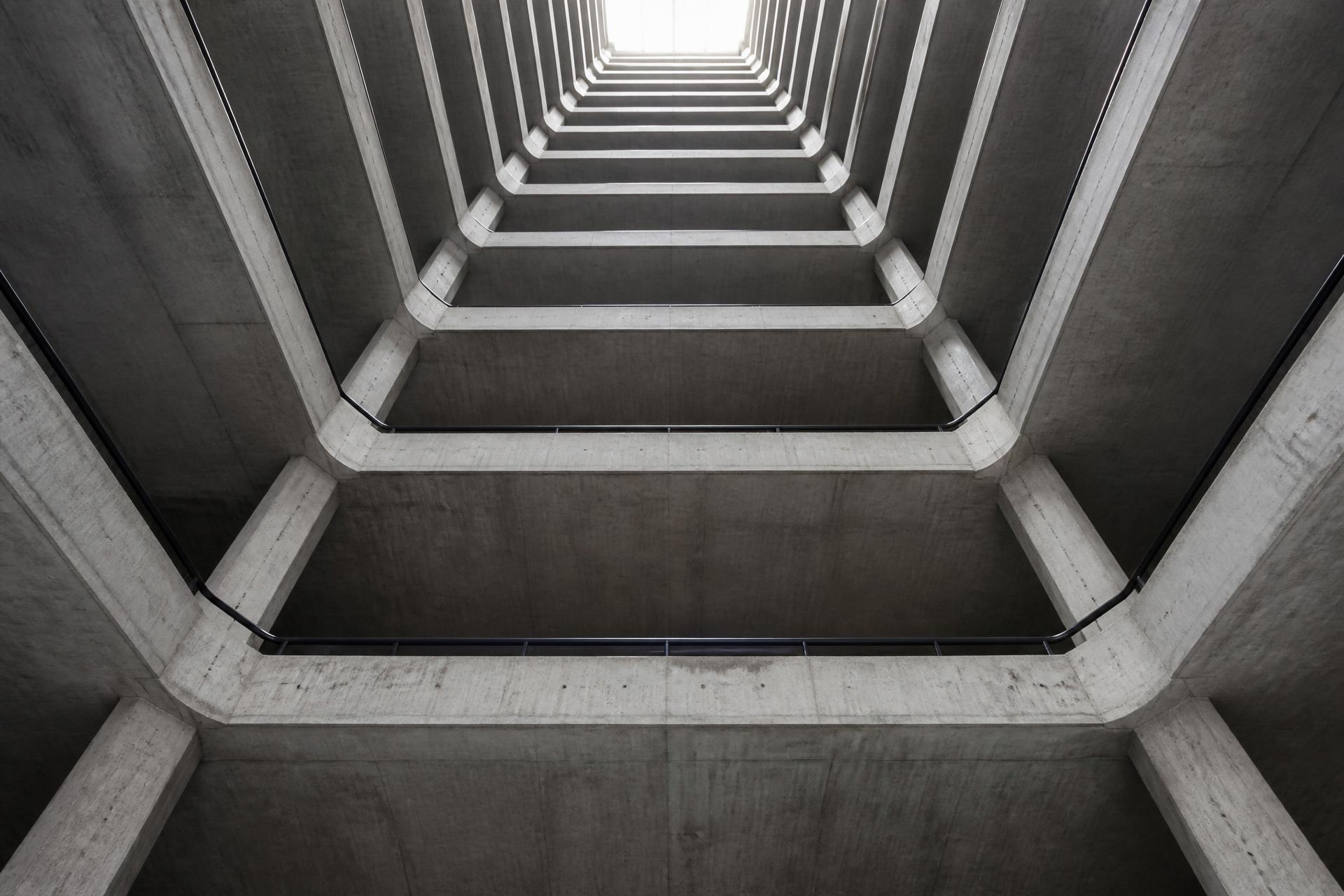 Circulação vertical de concreto fotografada de baixo, com geometria repetida até o topo